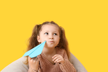 Cute little girl with paper plane on yellow background