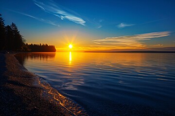 Obraz premium : A tranquil sunset at the coast of a serene northern European lake, where the blue sky meets the golden sunlight reflecting on the calm water, with silhouettes of distant pine trees on the horizon.