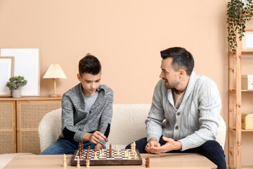 Father and his little son playing chess on sofa at home