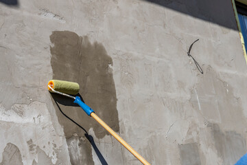 applying a primer to the wall with a yellow roller, showing the process of improving and repairing...