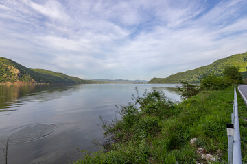 Fototapeta premium The calm water reflects the greenery and distant hills, with ripples suggesting recent activity. The daylight illuminates the scene, highlighting the ecological diversity and peaceful setting