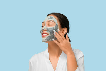 Young woman with clay mask on her face against blue background