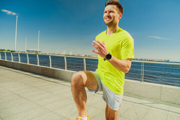 A man in a yellow shirt and shorts exercises outdoors on a sunny waterfront promenade, raising his...