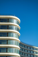 A modern, curved glass building with a clear blue sky in the background.