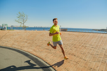 A man in a bright yellow shirt runs energetically along a waterfront path under a clear blue sky.