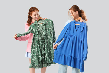 Happy redhead sisters with stylish dresses on grey background
