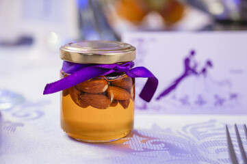 A small glass jar filled with a golden liquid, topped with a metallic lid and tied with a purple...