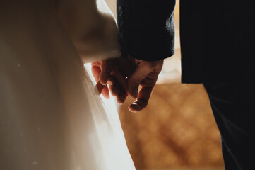 A tender moment between two individuals, presumably a couple, as they hold hands. The woman, on the left, wears a white garment, possibly a wedding dress, while the man, on the right