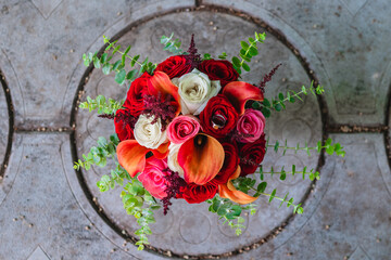 The bouquet consists of roses in varying shades of red, orange, and white, complemented by green...