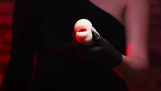 Sex toys for men. An artificial mouth-shaped masturbator made of silicone in the hands of a girl in black gloves and a black dress on a red background. Sex shop Adult store
