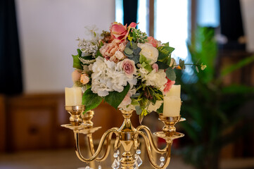 A beautifully arranged floral centerpiece placed on a golden candelabra. The candelabra has multiple arms, each holding a lit candle. The centerpiece is a mix of white and pink flowers, possibly roses