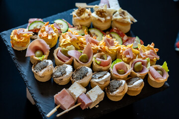 A platter of assorted canapés and skewered appetizers. The platter is dark, possibly made of slate or stone, and is placed on a reflective surface