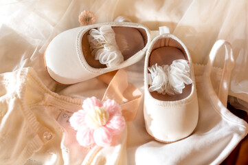 A pair of white baby shoes with delicate lace detailing. They are placed on a soft, light-colored...