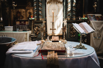 An ornate religious setting, possibly a church or cathedral. At the forefront, there's a table with a lit candle, a book, and other religious artifacts. Behind the table, there's a wooden altar