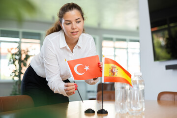 Positive young woman putting little flag of Turkey on table next to the flag of Spain and bottles...