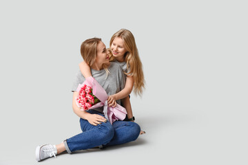 Cute little girl with her mom and bouquet for Mother's Day sitting on white background