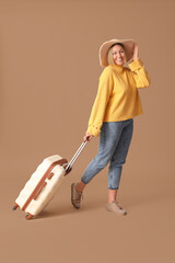 Young female tourist with suitcase on beige background