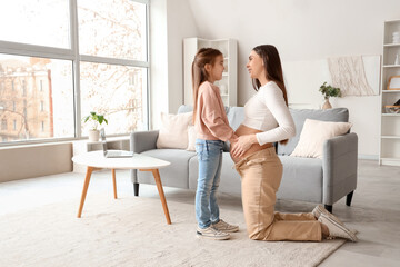 Young pregnant woman with her little daughter at home