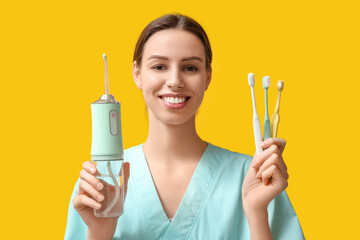 Female dentist with oral irrigator and toothbrushes on yellow background