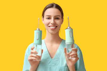Female dentist with oral irrigators on yellow background