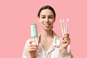 Beautiful young woman with oral irrigator and toothbrushes on pink background