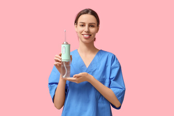 Female dentist with oral irrigator on pink background