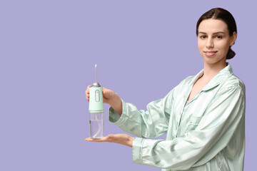 Beautiful young woman with oral irrigator on lilac background