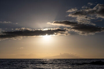 Dramatic sunset over the Pacific Ocean, sunbeams radiating out from behind clouds, island in the background, Maui, Hawaii
