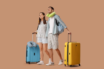 Beautiful young happy couple of tourists with suitcases, backpacks and travel pillows on brown...