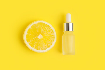 Bottle of citrus essential oil and fresh lemon on yellow background