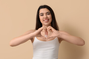 Happy smiling young woman holding crystal deodorant and making heart with her hands on beige...