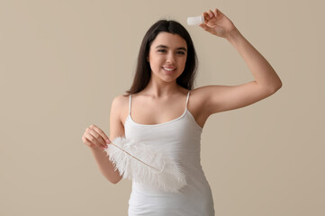 Happy smiling young woman with crystal deodorant and feather on beige background