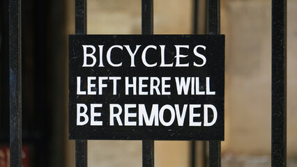 Close up of bicycles left here will be removed sign on metal fence gate on street of urban city