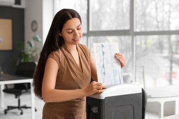 Young secretary destroying documents using shredder in office