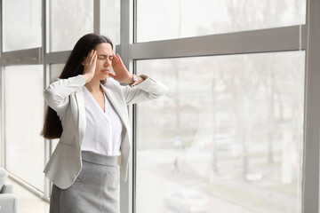 Young woman suffering from headache near window in office