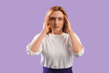 Upset adult woman suffering from headache on lilac background