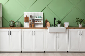 Interior of stylish kitchen with white counters, pegboard and green wall