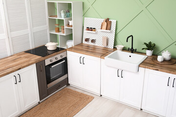 Interior of stylish kitchen with white counters, pegboard and green wall