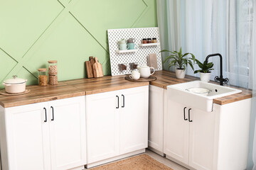 Interior of stylish kitchen with white counters, pegboard and green wall