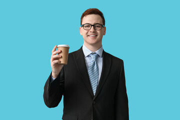 Young man in eyeglasses holding paper cup of coffee on blue background