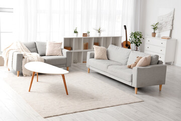 Interior of light living room with grey sofas, table and drawers