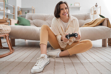 Young woman playing video game on floor near sofa in living room