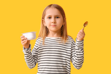 Cute little girl with spoon and yogurt on yellow background
