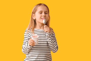 Cute little girl with spoon eating yogurt on yellow background