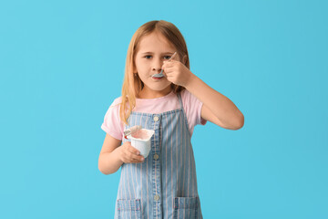 Cute little girl with spoon eating yogurt on blue background