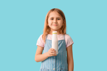 Cute little girl with bottle of yogurt on blue background