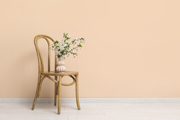 Blooming branches in vase on chair near beige wall
