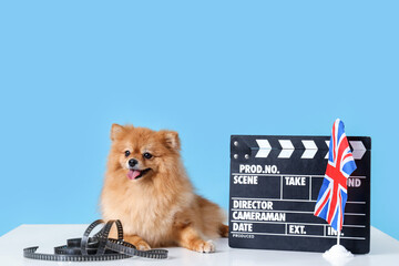 Cute Pomeranian dog with UK flag, film and movie clapper on table against blue background