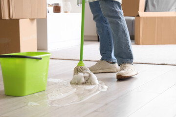 Young man mopping floor in kitchen on moving day, closeup