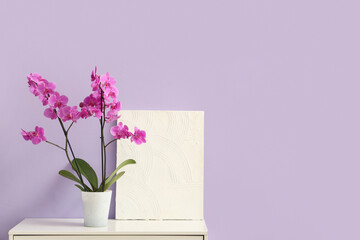 Orchid flower with painting on commode near lilac wall